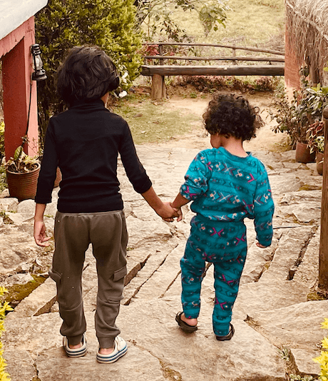 Two children walking hand in hand down a stone path at Kanav