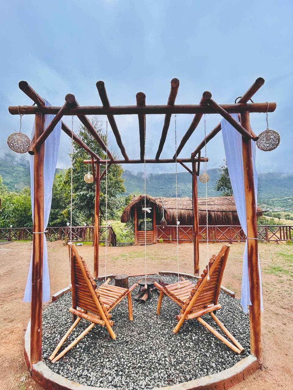 Two wooden chairs beneath a timber pergola, with thatched cottages and hills beyond