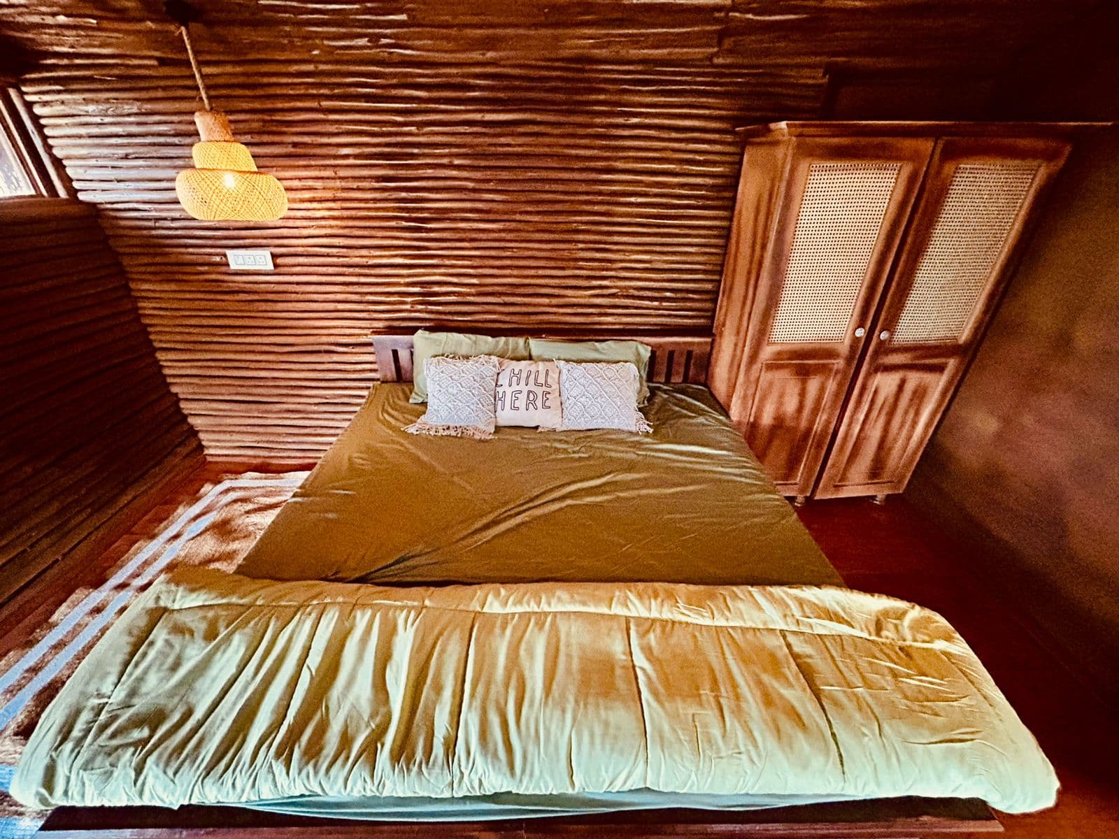 A wood-panelled bedroom with a rattan wardrobe and a woven pendant lamp